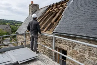 Couvreur inspectant la charpente d’une ancienne maison entre ardoises naturelles et échantillons de fibrociment.